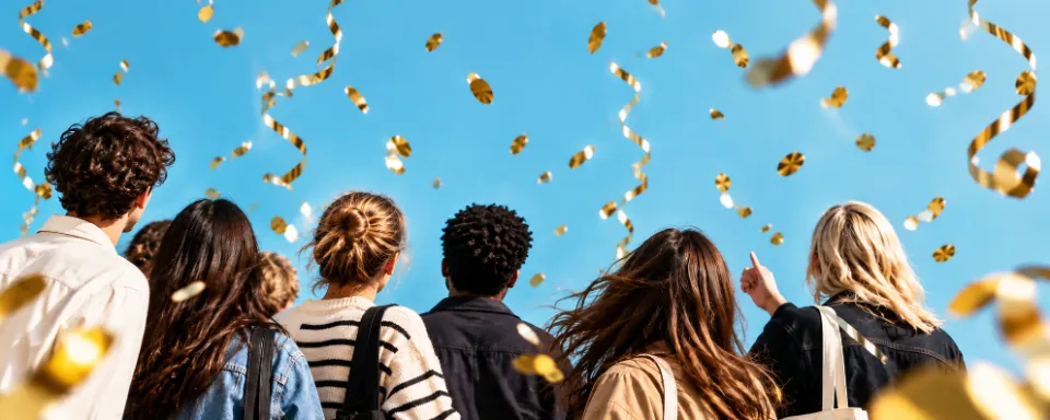 Friends looking up as gold confetti and streamers fall against a blue sky